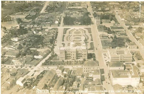 Vista aérea da Praça Santos Andrade, na metade da década de 1930. Envolta por uma consolidada malha urbana, a praça apresenta o paisagismo à francesa implantado em 1917 e complementado em 1922. Em primeiro plano, os edifícios da Universidade do Paraná e da Agencia de Correios e Telégrafos (Correio Velho).
